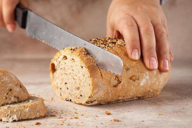 Mani del panettiere, tritare il pane ai cereali con il coltello, fette sul tagliere di legno, il concetto di colazione, orizzontale, copia spazio, posto per il testo