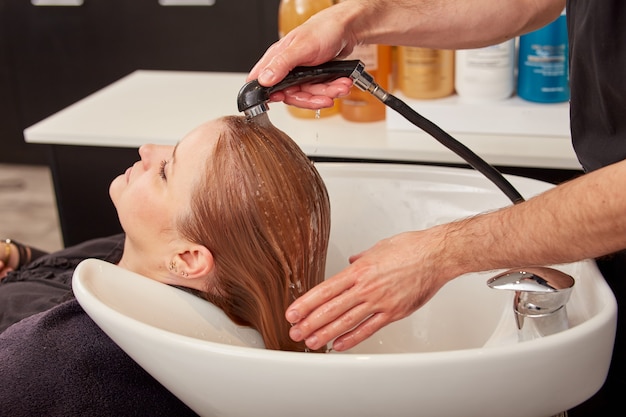 Mani del parrucchiere maschio che lavano i capelli della donna nel lavandino