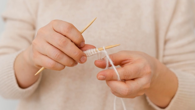 Mani del primo piano che lavorano a maglia con filo bianco