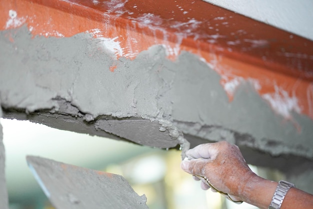 Mani del primo piano del costruttore che tengono la vaschetta del mortaio e intonacano le pareti con cemento nel cantiere