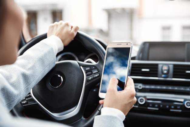 Mani del primo piano del driver femminile che si siede in una macchina e utilizzando il telefono cellulare.