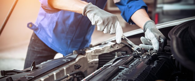 Mani del primo piano del meccanico automatico che utilizzano la chiave per la manutenzione del motore dell'auto