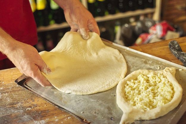 Mani del primo piano del panettiere maschio che preparano khachapuri georgiano tradizionale di cucina