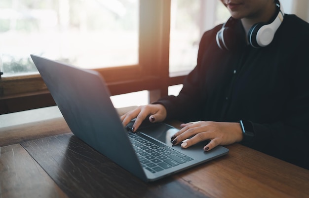 Mani del primo piano della donna imprenditrice freelance di affari con la cuffia bianca che lavora digitando la tastiera sul computer portatile e sulla tavola di legno alla caffetteria del caffè Concetto di tecnologia aziendale