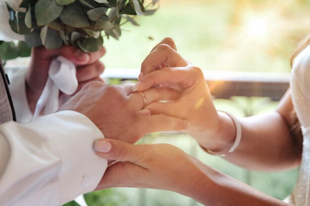 Mani del primo piano della fidanzata della sposa che tengono la mano dello sposo e che mettono l'anello nuziale sul dito alla persona amata