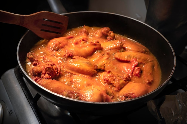 Mani del primo piano della giovane donna latina che cucina pollo e spezie in salsa barbecue a casa