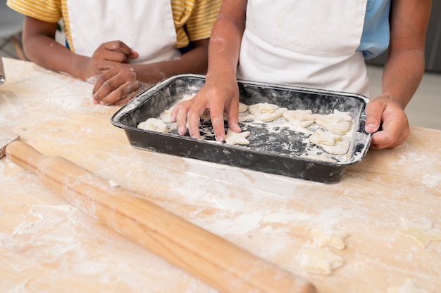 Mani del ragazzo che tagliano i biscotti dall'impasto arrotolato mentre cucinano la pasticceria per la cena di Natale