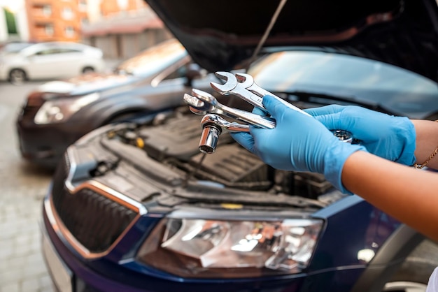 Mani del riparatore del meccanico di automobile che riparano il motore dell'automobile dell'officina dell'automobile con la chiave e servizi di riparazione di servizio dell'automobile