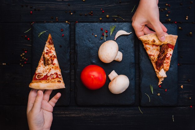 Mani del `s del bambino e pizza fresca su una tavola di legno nera