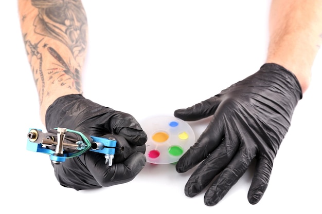 Mani del tatuatore in guanti neri con macchinetta per tatuaggi e inchiostri colorati isolati su sfondo bianco da vicino