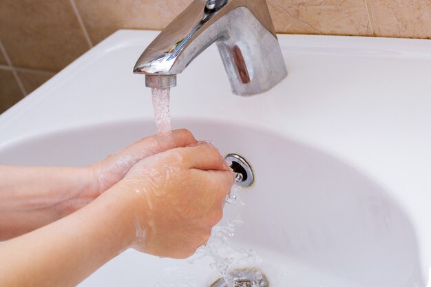Mani delicate che si lavano sotto il rubinetto sopra il lavandino bianco