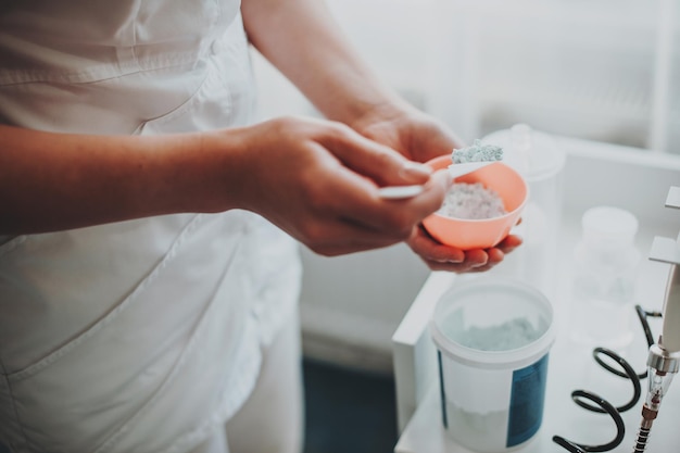 Mani dell'estetista che preparano una maschera idratante per applicare il trattamento del viso della procedura di cura della pelle dei volti delle donne...