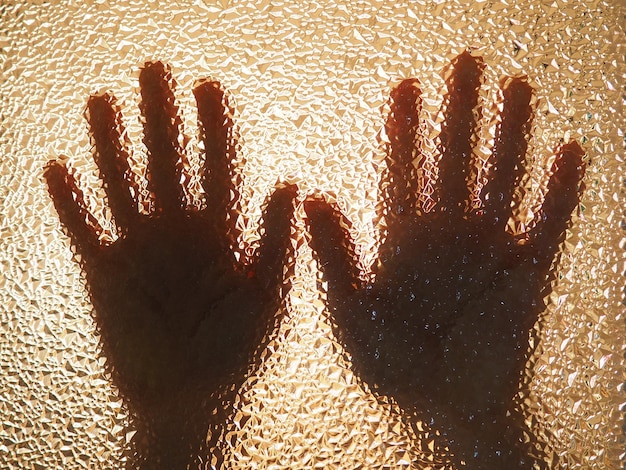 Mani dell'orrore. Le mani ombra dell'essere umano dietro il vetro. Vetro strutturato ondulato attraverso il quale sono visibili i palmi dei bambini.