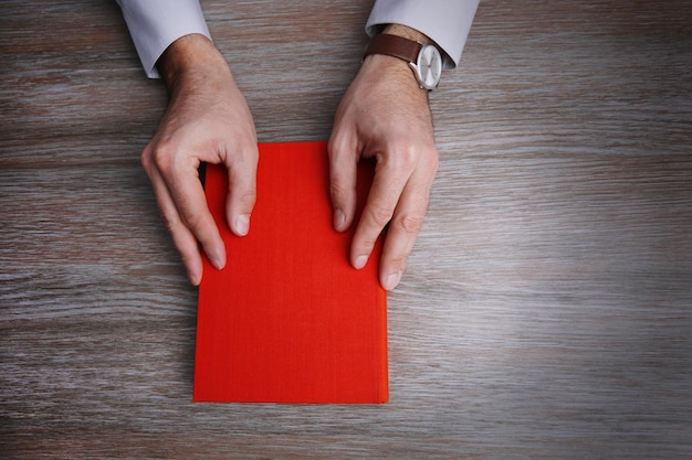 Mani dell'uomo che tengono libro sul fondo della tavola in legno