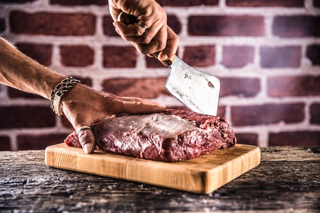 Mani dell'uomo del macellaio che tagliano la bistecca di manzo cruda in macelleria.