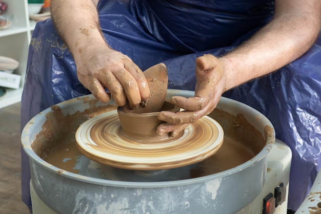 mani dell'uomo senior della ceramica che scolpiscono dall'argilla sulla pentola della ruota di ceramica in officina