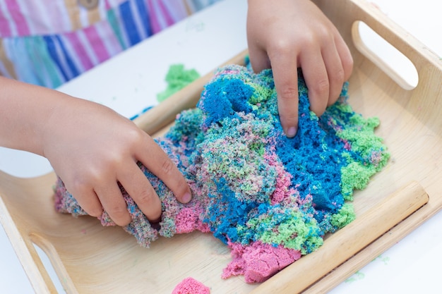 Mani della bambina che giocano con il primo piano cinetico della sabbia. Attività per il tempo libero all'aperto in giornata estiva.