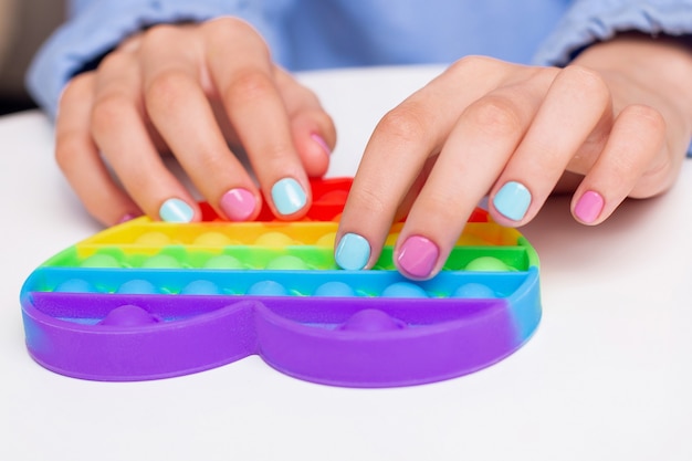 Mani della bambina con bellissime unghie per manicure che tengono un giocattolo pop it