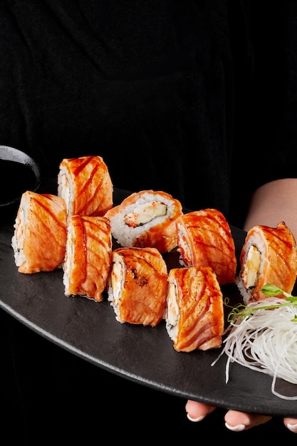 Mani della cameriera che tengono piatto con rotolo di sushi con crema di formaggio di salmone scottato tobiko rosso e mela