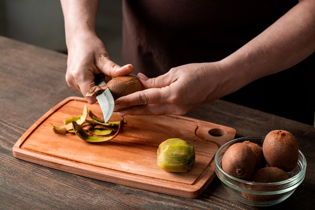 Mani della casalinga che sbucciano kiwi freschi sul tagliere dal tavolo della cucina mentre li prepara per affettare e asciugare per l'inverno
