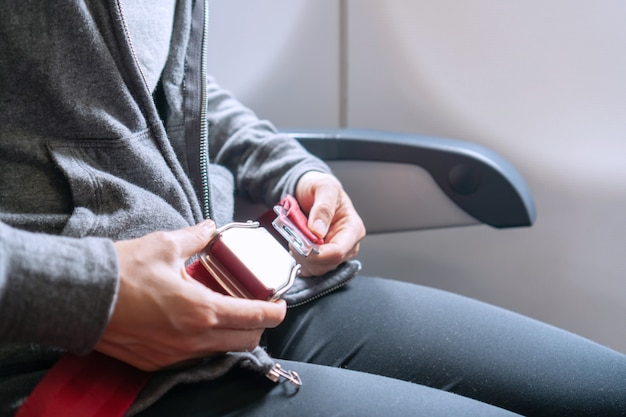 Mani della cintura di sicurezza di fissaggio passeggero donna asiatica mentre è seduto sull'aereo. Concetto di viaggio.