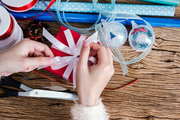 Mani della donna che avvolgono il contenitore di regalo rosso con il nastro bianco