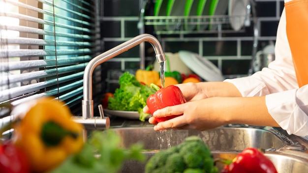 Mani della donna che lavano le verdure per la preparazione dell'insalata vegana