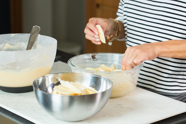 Mani della donna che mettono le mele durante la cottura della torta di mele