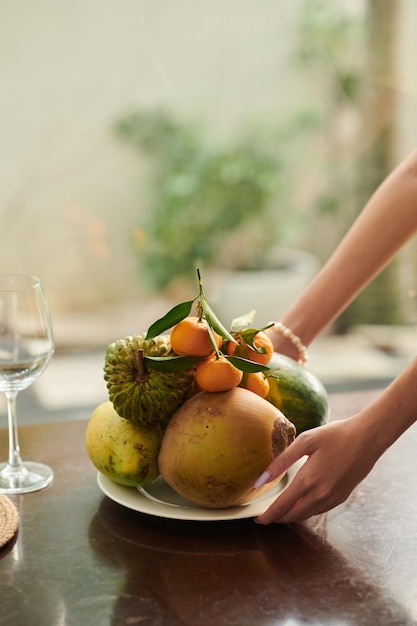 Mani della donna che mettono piatto con frutta fresca sul tavolo da pranzo