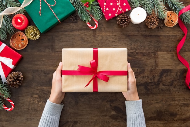 Mani della donna che mostrano il contenitore di regalo di Natale sulla tavola di legno