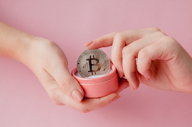 Mani della donna che tengono bitcoin in confezione regalo rosa su sfondo rosa, simbolo di denaro virtuale