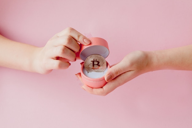 Mani della donna che tengono bitcoin in confezione regalo rosa