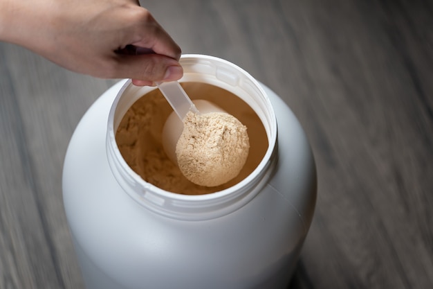 Mani della donna che tengono misurino di polvere di proteine del siero di latte sopra il barattolo.