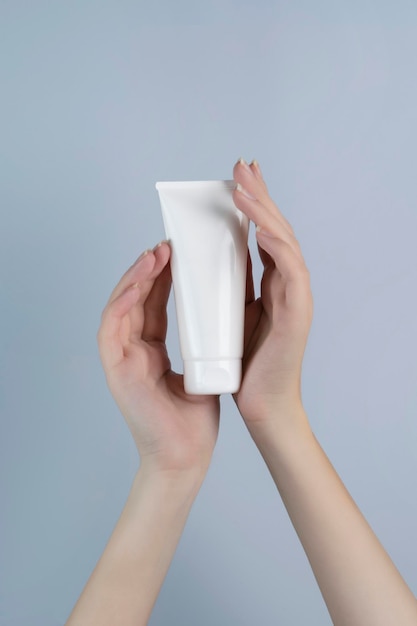 Mani della donna che tengono un tubo di crema bianca Mockup di cosmetici