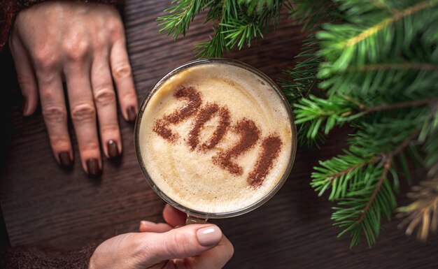 Mani della donna che tengono una tazza di caffè con 2021 sulla schiuma di latte alla cannella