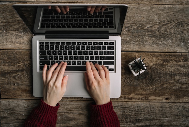 Mani della donna con il computer portatile che lavora al fondo di legno