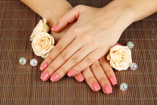 Mani della donna con manicure rosa e fiori su sfondo stuoia di bambù