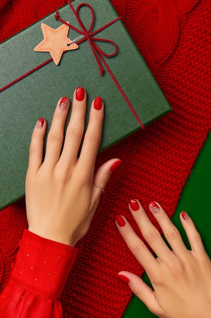 Mani della donna con manicure rossa alla moda con confezione regalo su coperta a maglia manicure pedicure salone di bellezza...