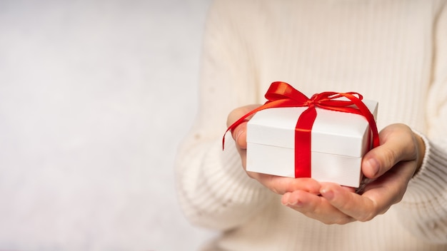 Mani della donna di bellezza che tengono il contenitore di regalo con l'arco rosso