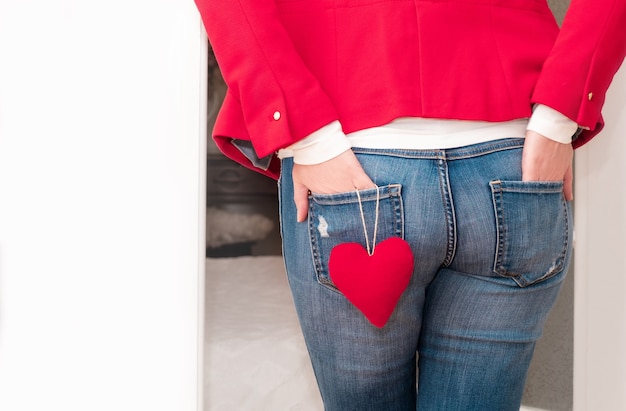 Mani della donna nelle tasche posteriori dei jeans con un grande cuore rosso di San Valentino vicino alla porta bianca.