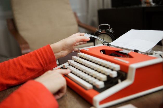 mani della donna sulla macchina da scrivere rossa dell'annata con carta bianca sullo scrittorio di legno