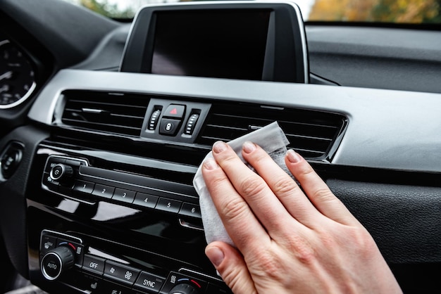 Mani della giovane donna che puliscono la polvere dell'auto con un panno umido bianco.