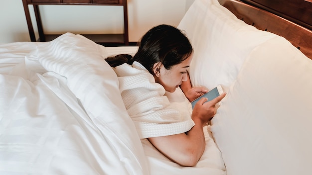 Mani della giovane donna che tengono lo smartphone a letto dopo il risveglio.