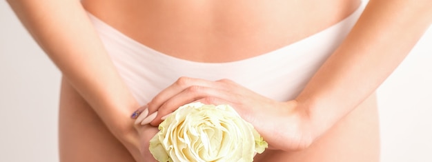 Mani della giovane donna che tiene un fiore bianco che copre zona bikini epilate isolato su sfondo bianco studio concetto di ginecologia riproduttiva di salute femminile
