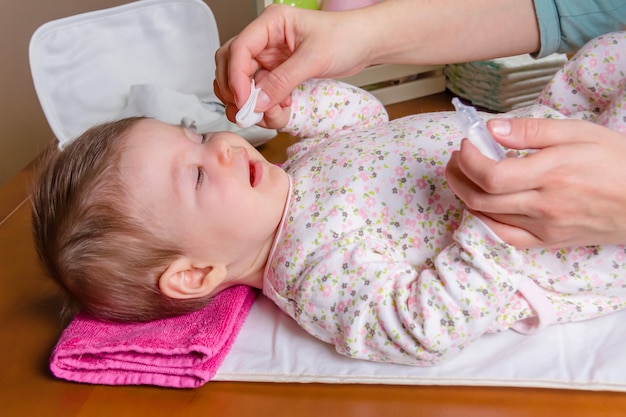 Mani della madre che puliscono gli occhi del bambino con siero fisiologico in un batuffolo di cotone