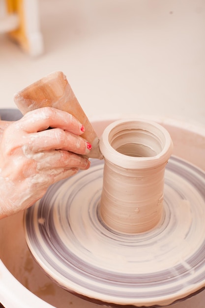 Mani della ragazza che fa la ceramica dall'argilla bianca su un tornio da vasaio