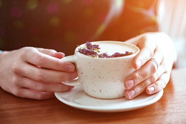 Mani della ragazza che tengono una tazza di cappuccino