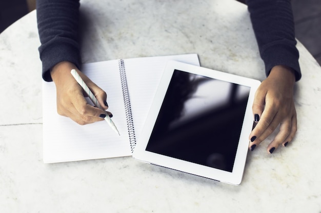 Mani della ragazza con tavoletta digitale e diario in bianco