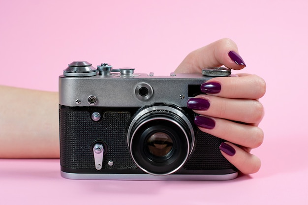 Mani della ragazza e fotocamera su uno sfondo rosa