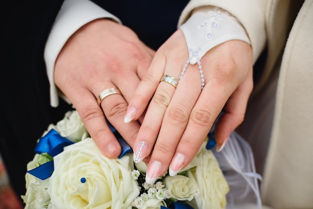Mani della sposa e dello sposo con anelli di nozze d'oro di un bellissimo bouquet